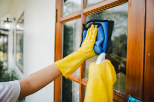 Hand in gelben Gummihandschuhen reinigt ein Fenster mit einem blauen Reinigungstuch.