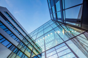 Moderne Glasfassade eines Bürogebäudes mit reflektierenden Fenstern, die den Himmel widerspiegeln. Eine Herausforderung für die professionelle Fensterreinigung.