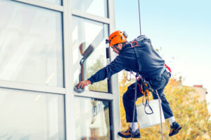 Reinigungskraft mit Sicherheitsausrüstung reinigt ein Fenster in großer Höhe von außen.