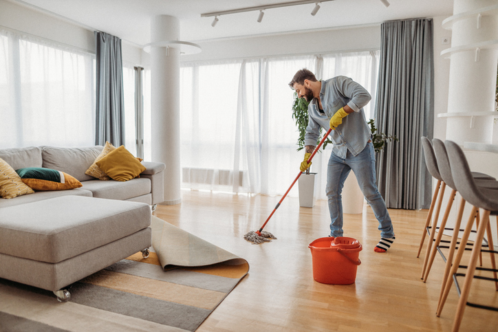 Mann wischt den Boden in einem modernen Wohnzimmer mit gelben Gummihandschuhen