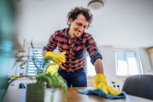 Mann reinigt professionell einen Tisch in einem modernen Wohnzimmer mit gelben Gummihandschuhen und einem blauen Tuch