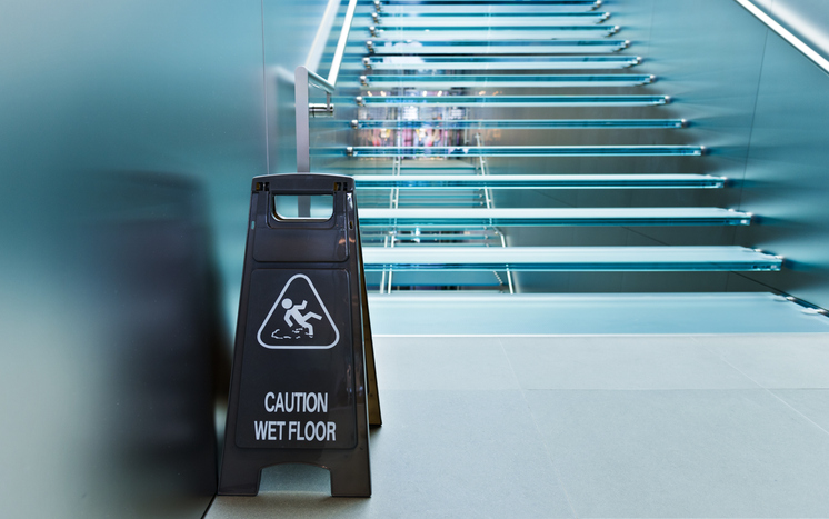 Warnschild ‚Caution Wet Floor‘ vor einer Treppe – Hinweis auf Sicherheit bei der Treppenhausreinigung.